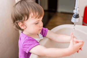 Kleines Kind steht am Waschbecken und hält die Hände unters Wassser